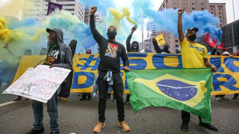 تظاهرکنندگان با ماسک صورت در خیابان پائولیستا در جریان اعتراض به همه‌گیری ویروس کرونا (COVID-19) در 14 ژوئن 2020 در سائوپائولو، برزیل، مشت خود را بالا می‌برند.